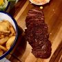 Iron Lady - dat komende week officieel opent in de Pannekoekstraat - mikt op slechts een stuk vlees: de flat iron steak. Volop tegen de vega(n) wind in geven de ondernemers die eerder van Sugo een succes maakten een eigen draai aan het concept van Flat Iron uit Londen, de Europese food hoofdstad. 
Flat iron steak? Ja, dat is een deel van de schouder van de koe, dat vroeger in de VS, waar deze cut al even aan een opmars bezig is, in de hamburger ging. Want het is smaakvol maar wel taai. Inmiddels snijden de slagers dit stukje anders uit en verwijderen ze de zenen. Zo ontstaat een mals stukje vlees, dat qua vorm wat weg heeft van een strijkijzer. Vandaar de naam.

De flat iron steak wordt eigenlijk altijd getrancheerd opgediend. Bij Iron Lady (waarom de zaak vernoemd is naar de Britse premier die gangmaker is van 40 jaar neoliberalisme is me niet duidelijk) vul je de steak aan met sides zoals friet, zoete aardappel friet en een trits aan groentengerechtjes. Voor de vegans is er een beyond meat burger en voor de mensen die de flat iron steak zat zijn een bavette (ook minder bekende steak met veel smaak) en een ouderwetse burger op een brioche. Voeg daar een dessert aan toe (een eigentijdse variant op de dame blanche) en je kent het hele menu van Flat Iron.

Iron Lady biedt de flat iron steak aan voor de bizar lage prijs van €11 en dan is het vlees van Nice to meat, dus zeker geen rotzooi. Met 2 sides en 2 drankjes ben je dan voor onder de €25 klaar. Dan begin je bij de meeste vleesrestaurants net aan je hoofdgerecht. 
#pannekoekstraat #flatironsteak #debuikvanrotterdam #newrestaurant