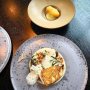 Waar moet je hier nu kijken? Getrainde Hollandse ogen schieten direct naar de kibbeling, de fine dining amateur treft de heilbot met Hollandse garnalen, bloemkool en pernodsaus. Het voordeel is dat je niet hoeft te kiezen. De beide bordjes zijn familie: de kibbeling is gemaakt met - hoe zeg je dat netjes - het afval van de heilbot. Zo ontstaat hier een fijn spel tussen “Dutch streetfood” en chique(r) dineren. Chef Sander Bierenbroodspot, verantwoordelijk voor alles in de keuken van het prettig gestoord ingerichte Andaz hotel, heeft deze combi nog even op het menu staan bij Bluespoon, dus wees er snel bij. 
#debuikvanamsterdam #prinsengracht #andazamsterdam #kibbeling #streetfood #bluespoonamsterdam